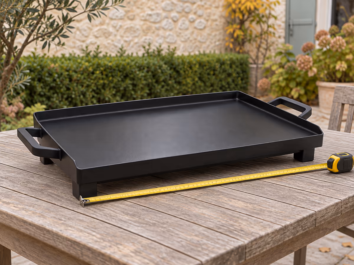 Plancha de table noire posée sur une table de jardin en bois, mètre ruban déroulé le long de la plaque pour relever la longueur