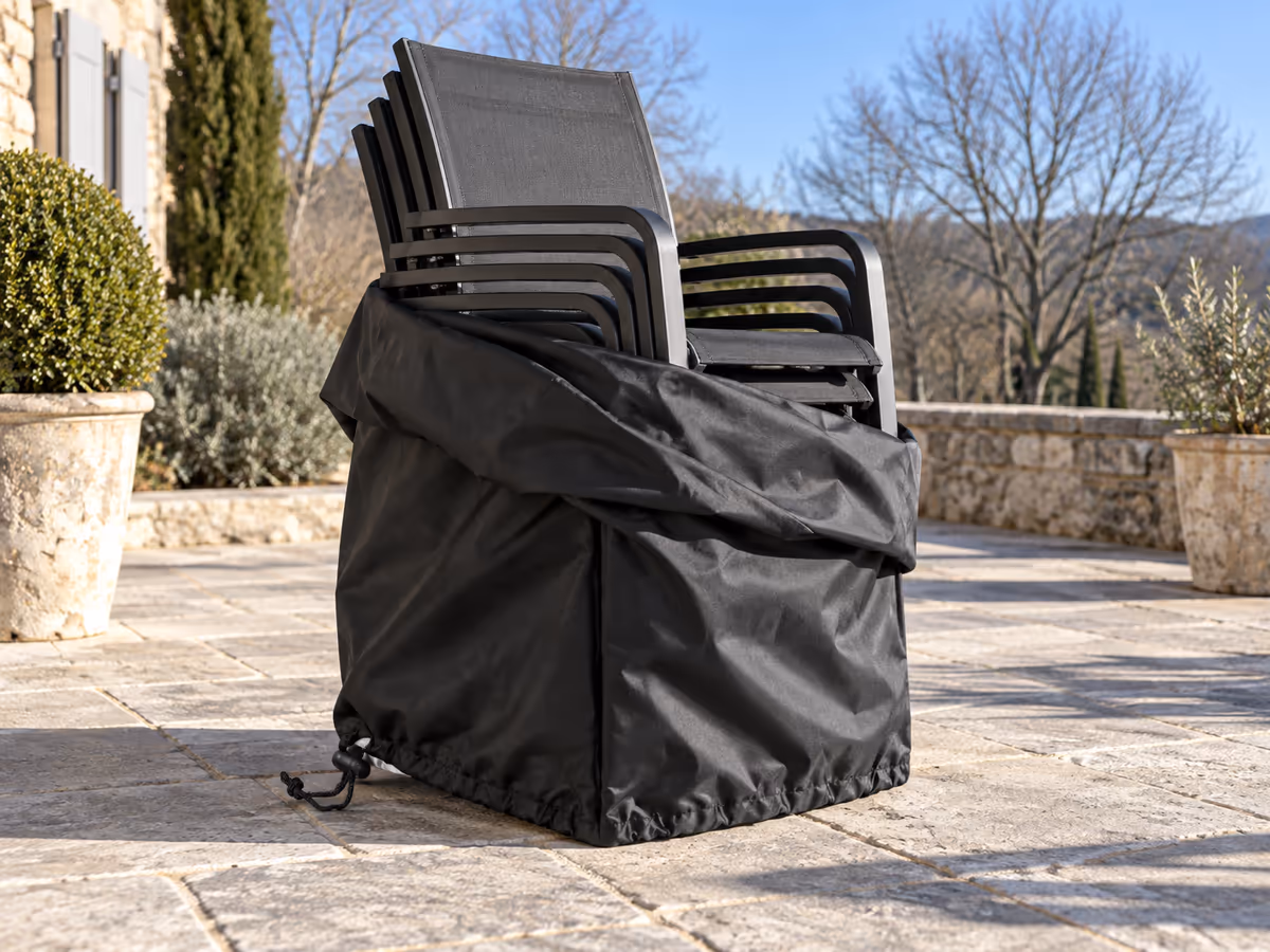 Housse soulevée à moitié sur une pile de chaises par une journée d'hiver ensoleillée, ombre nette sur les dalles de la terrasse