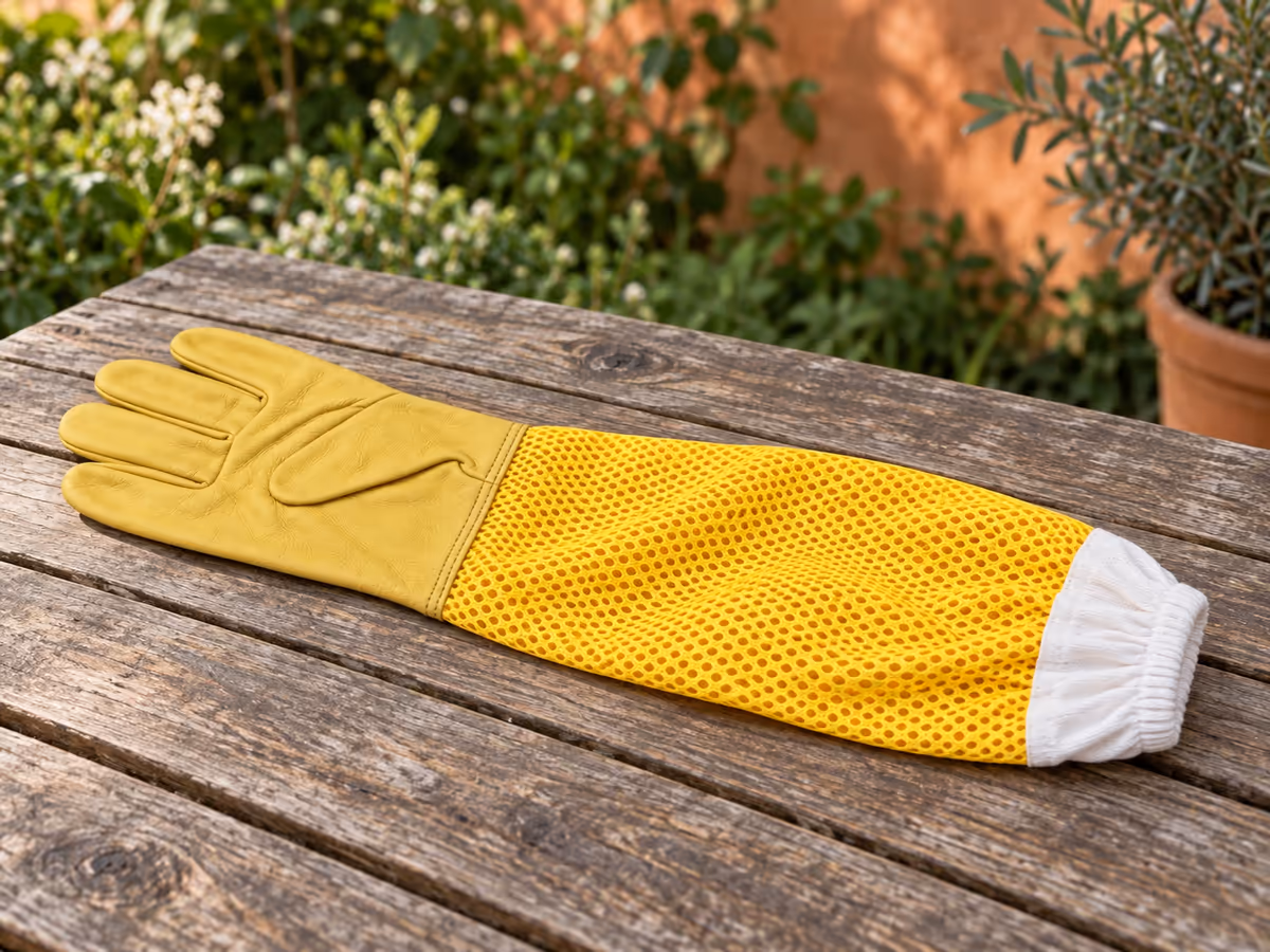 Manchon en filet jaune à mailles ovales posé à plat sur une table de jardin, poignet tricoté blanc rabattu à l'extrémité