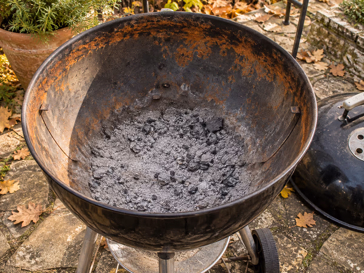 Intérieur d'une cuve de gril à charbon noire avec des auréoles de rouille orangée autour du bol, par une lumière d'automne