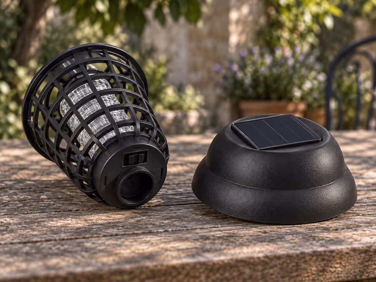 Tête de lampe solaire ouverte posée sur une table de jardin en bois, capot retiré, sélecteur à trois positions visible sous la cage métallique