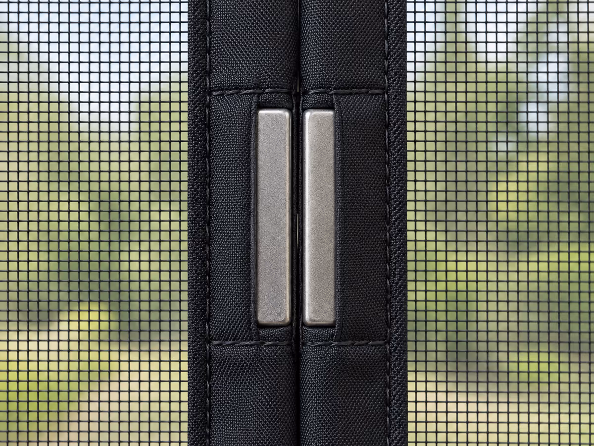 Détail de la rangée d'aimants rectangulaires cousus dans les bords des deux pans d'un rideau moustiquaire noir, couture fermée sur toute la hauteur
