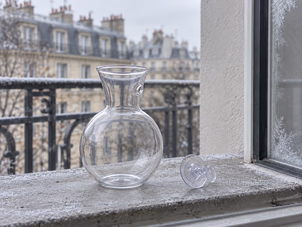 Vase mural transparent vide décroché de la vitre, posé sur un rebord de balcon avec des traces de givre sur le carreau