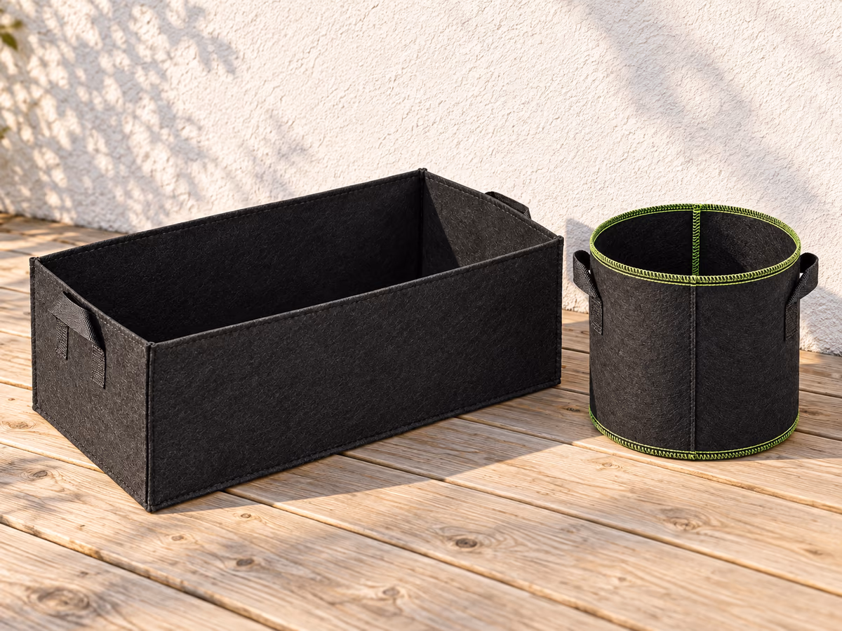 Un bac textile rectangulaire de 50 cm contre un mur de terrasse, un pot en tissu noir plus petit posé à côté, tous deux vides