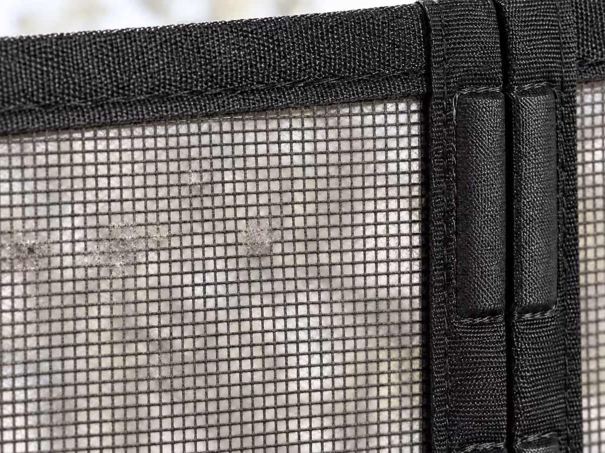 Gros plan sur la maille noire d'un rideau moustiquaire, fines poussières retenues entre les fils contre la lumière du jour