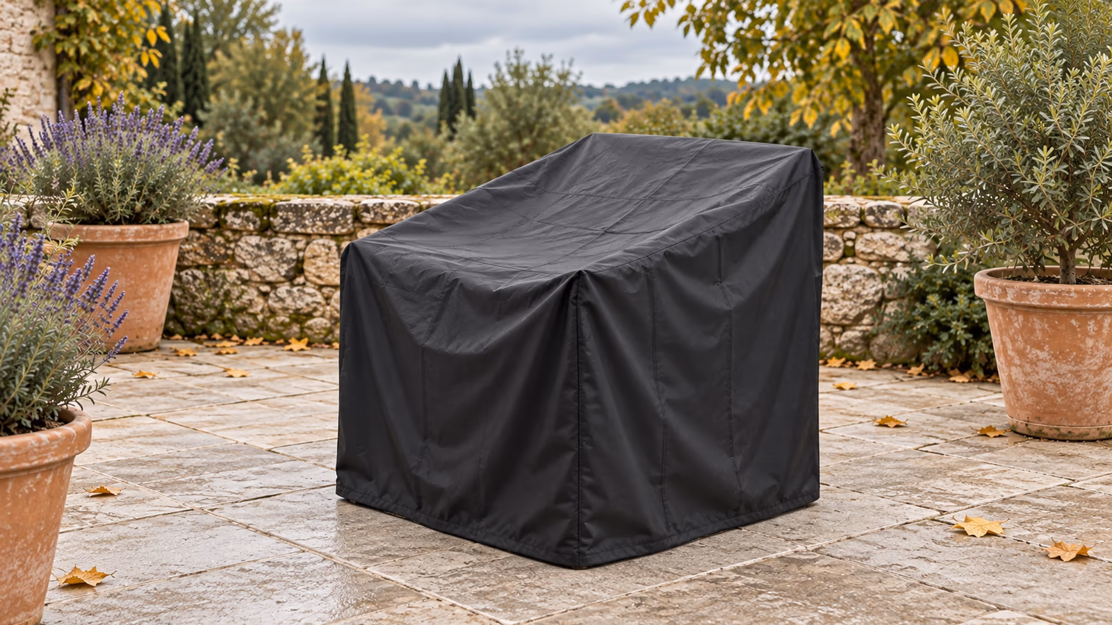 Housse de protection noire déployée sur un fauteuil de jardin compact en résine tressée, retombée descendue jusqu'aux dalles sur une terrasse d'automne
