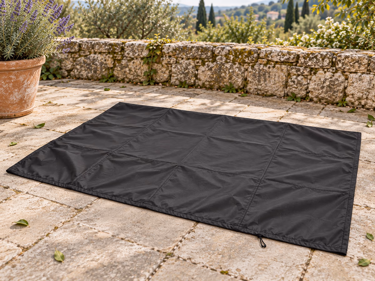 Housse de protection noire étalée à plat sur une terrasse au printemps pour sécher, cordon rentré dans l'ourlet, avant le pliage